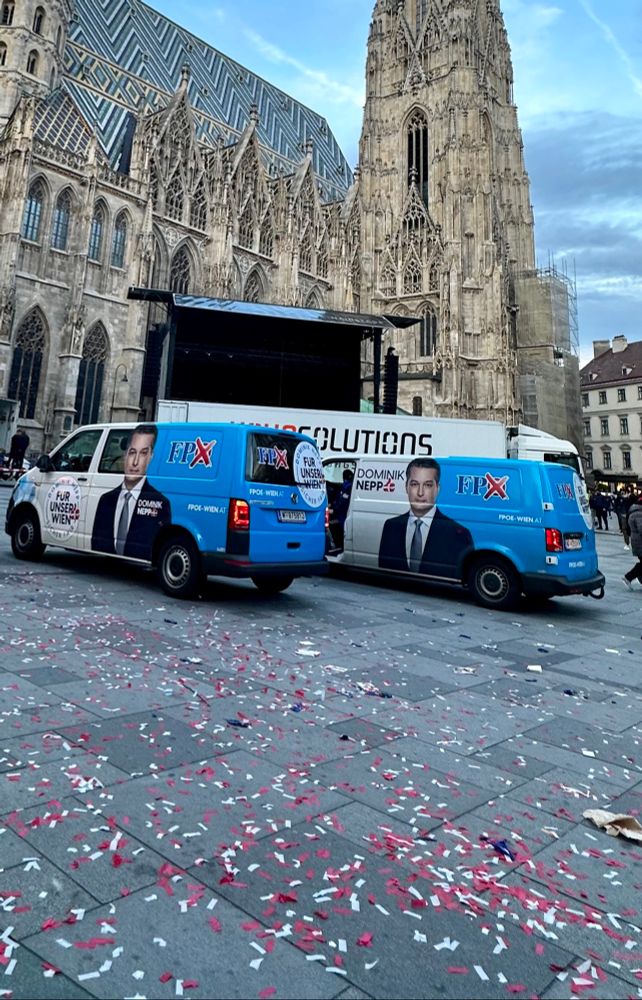 Foto zeigt einen Teil des Stephansplatz /Stephansdom mit einer verlassenen Bühne, zwei Werbebusse der FPÖ mit einem großen Foto von Dominik Nepp und ganz viele rote und weiße Schnipsel verstreut und durcheinander am Boden verstreut. Foto: @uebersleben 