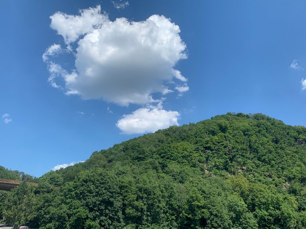 A white cloud quietly rises from the mountain peak, as if born from the mountain itself, slowly drifting toward the sky.