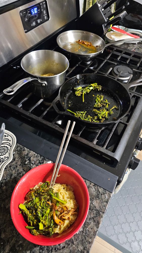 A bowl of chanterelle mushroom and broccolini ramen, next to a stove top showing the individual ingredients in 3 separate pans / pots