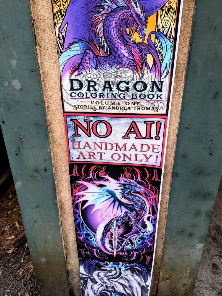 Art of two dragons is up on a wall, the top dragon being on the cover of a coloring book containing stories by Andrea Thomas. The middle displays the message "No AI! Handmade art only!"