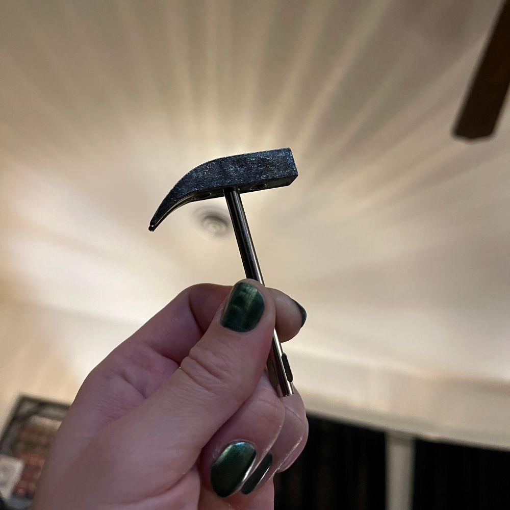 Photo of a small finger-sized square metal hammer. 