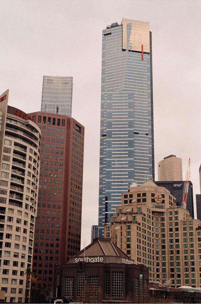 A large glass skyscraper with a gold and red accent overlaid atop the top few floors