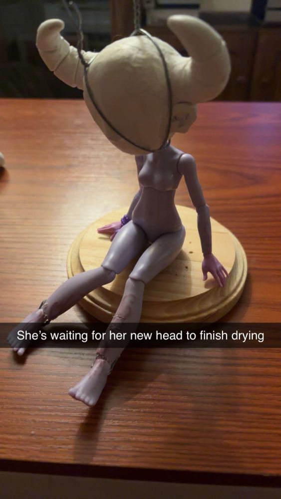 A Monster High doll body sitting on a wooden disk with a polymer clay head wired on