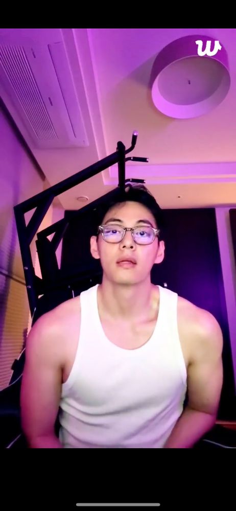 A screenshot of Kim Taehyung's last WeVerse live on June 20, 2025. He is wearing a white tank and glasses. He is directly facing his computer screen and showing off his muscles. 
