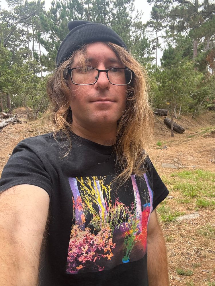 Selfie in forest with dirt, grass, trees, and overcast sky in background. I’m wearing a Hüsker Dü - Warehouse: Songs and Stories shirt.