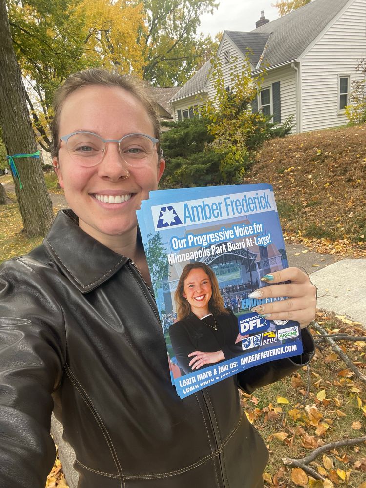 Amber standing and smiling with pieces of campaign lit amongst gorgeous fall trees