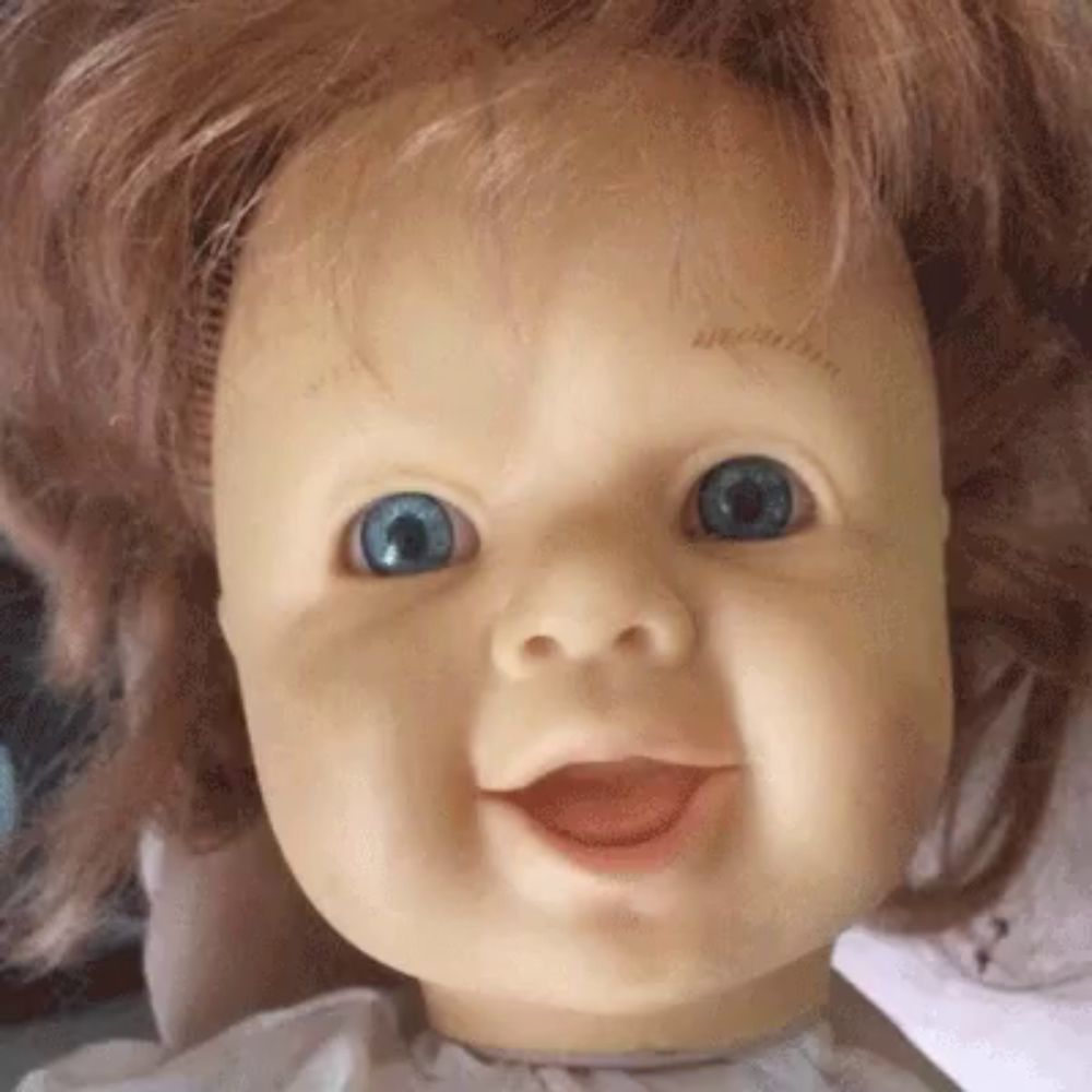 a close up of a doll 's face with blue eyes smiling .