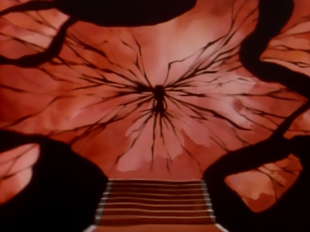 A screenshot of Anthy from episode 34 of Shoujo Kakumei Utena/Revolutionary Girl Utena, pierced by millions of twisted swords.