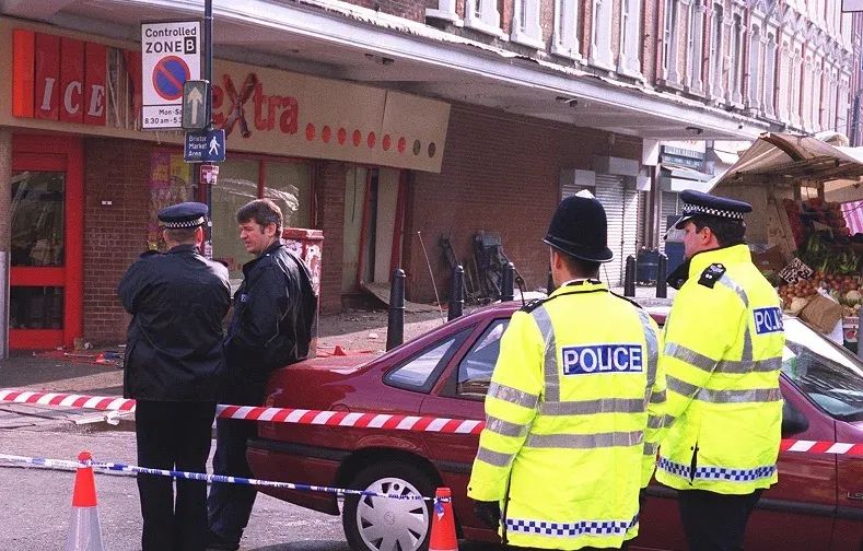 Police survey the damaged Iceland shopfront in the aftermath of the nailbomb explosion.