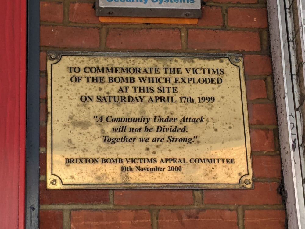 A commemorative plaque to the victims of the Brixton nail bombing. It reads: TO COMMEMORATE THE VICTIMS OF THE BOMB WHICH EXPLODED AT THIS SITE ON SATURDAY APRIL 17TH 1999. "A Community Under Attack will not be Divided. Together we are Strong." BRIXTON BOMB VICTIMS APPEAL COMMITTEE 10th November 2000.