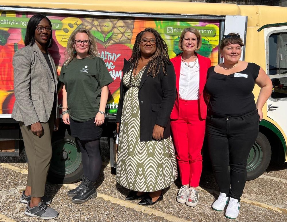 Florence Eshalomi, Bell Ribeiro-Addy and Helen Hayes stand with Healthy Living Platform volunteers in front of a truck with a Healthy Living Platform mural spraypainted onto the side shutter.