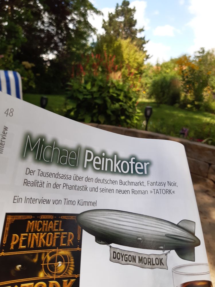 Eine Seite des Magazins phantastisch! mit der Überschrift Michael Peinkofer.
Auch ein Zeppelin und das Buchcover des RomansTatork. Im Hintergrund ein Gartenidyll.