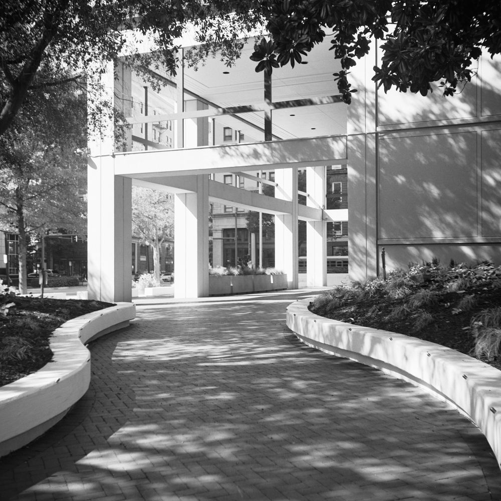 A black and white image of a path leading to the Federal Building.  Its a brick path with cement walls to each side. There's also an open design to the 1st floor.