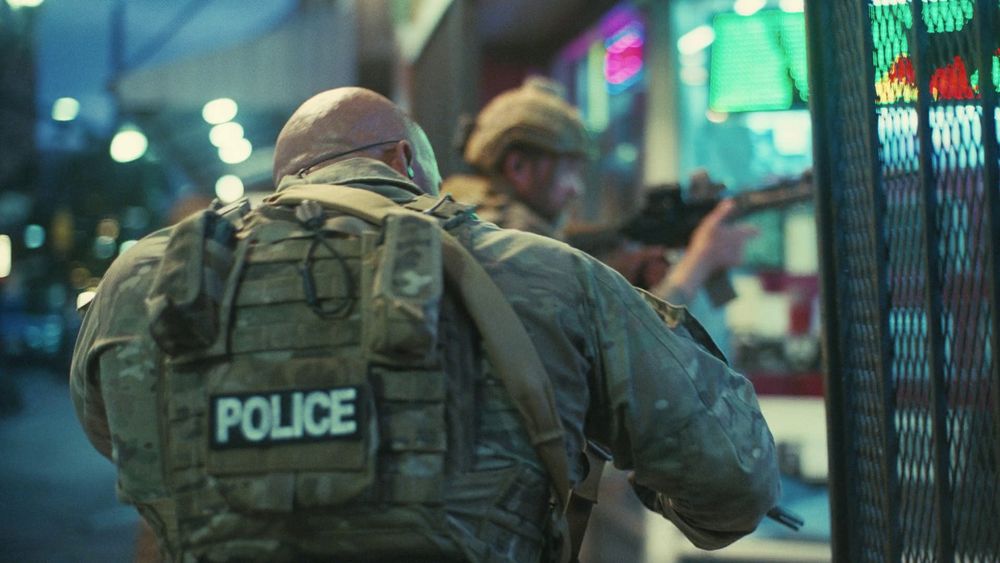 The many hues of a vibrant street. Men dressed for war. Redundantly stitched plate carriers and camouflage patterns. In white majuscule, "POLICE" is branded on them. One has his rifle raised as if its use was imminent.