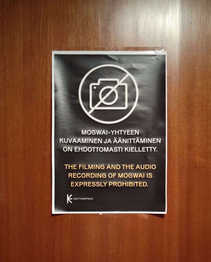 A poster with text "the filming and the audio recording of Mogwai is expressly prohibited" in Finnish and English