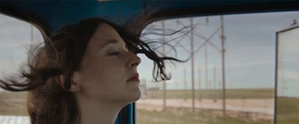 a woman with her eyes closed looks out a window with her hair blowing in the wind