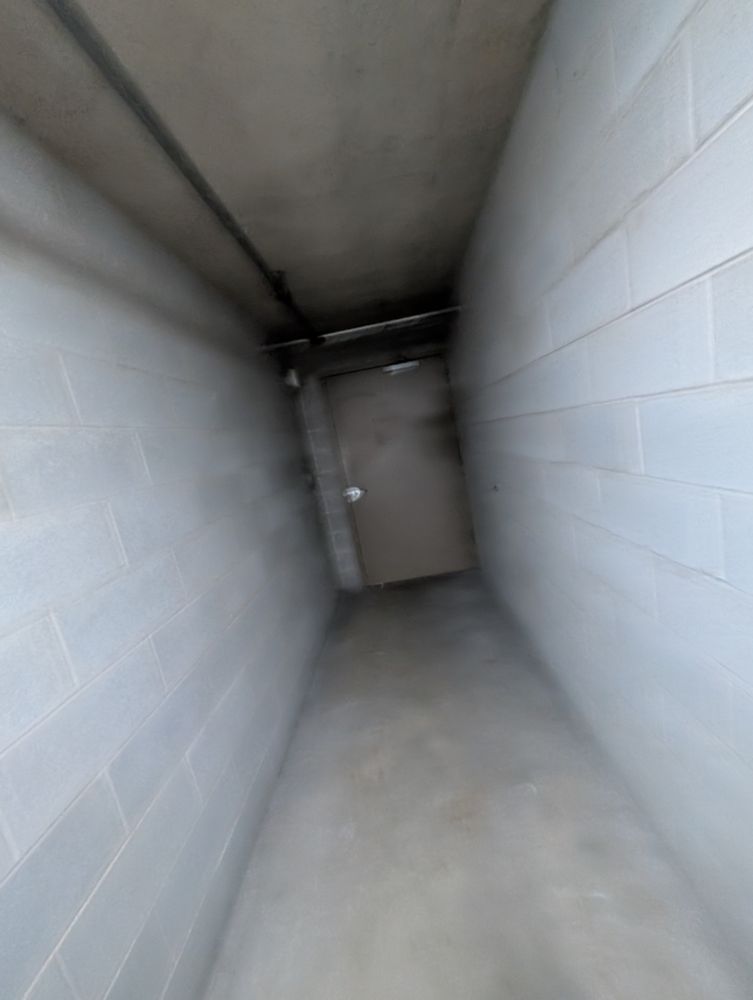 shaky image of a poorly lit concrete hallway with a shut door at the end