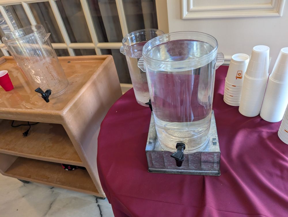 an extremely well used and busy hydration station with open jugs of water