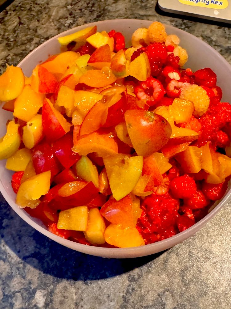 a bowl of cut bright yellow plums and red raspberries 