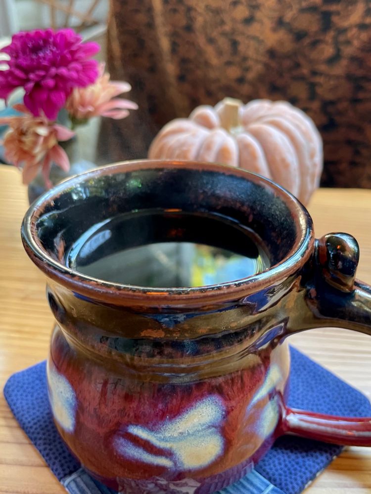 A colorful pottery mug of dark tea, pumpkin and flowers in the background 