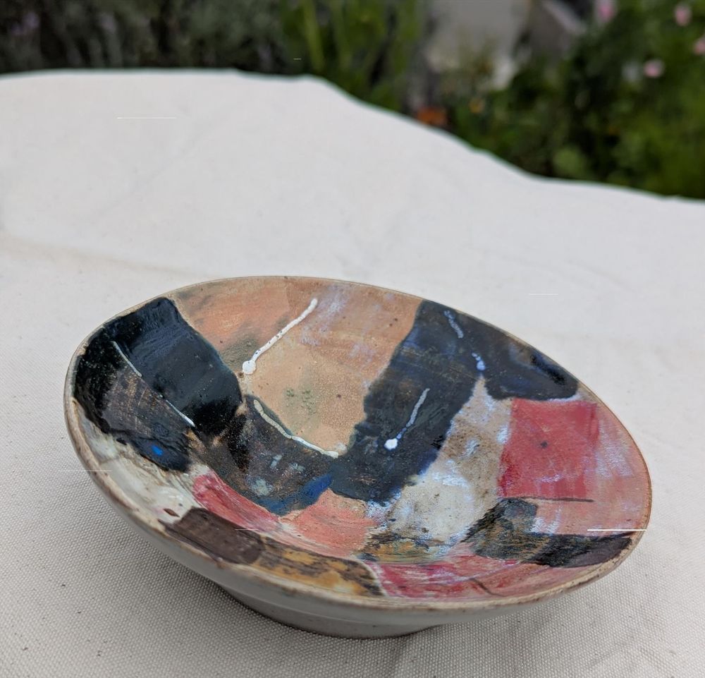 Eine bunter kleine Schale, angemalt mit Rechtecken in braun und rot Töne , ein bisschen Weiss und Blau, 
fotografiert auf einem hellen Hintergrund