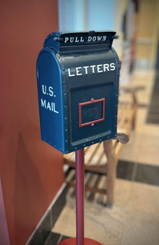 Old US postbox in dark blue made of sheet metal bearing the text "U.S. Mail", "Letters" and "Pull Down" on the opening. 