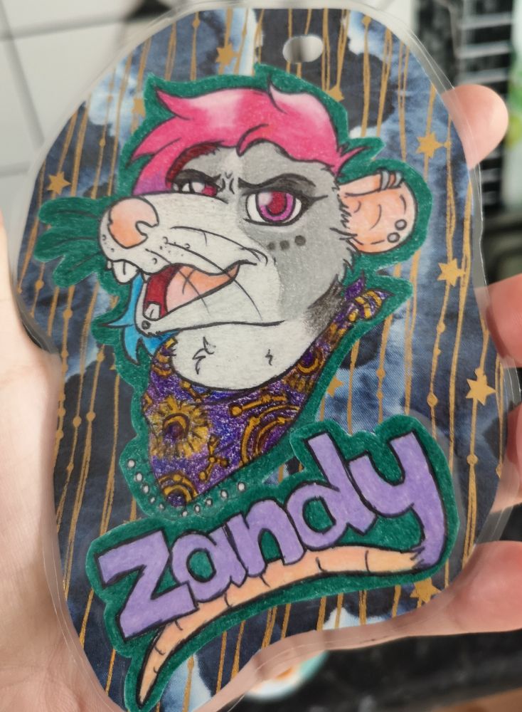 Character badge. Pencil crayon coloured headshot of a grey rat with a light grey muzzle and chest. She has pink eyes, fabulous pink hair with blue ends, and is wearing a purple bandana with a moon and stars type pattern. The name is underneath and outlined in dark green