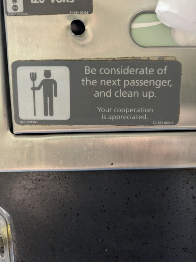 A sign in a train bathroom requesting you clean up after yourself with a pictogram of a man with horns and a pitchfork (or a hat and broom I guess)