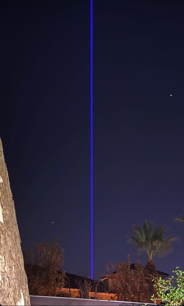 A bright purple ray of light shoots up from a building into the night sky. The beam’s light carries up throughout the entire shot