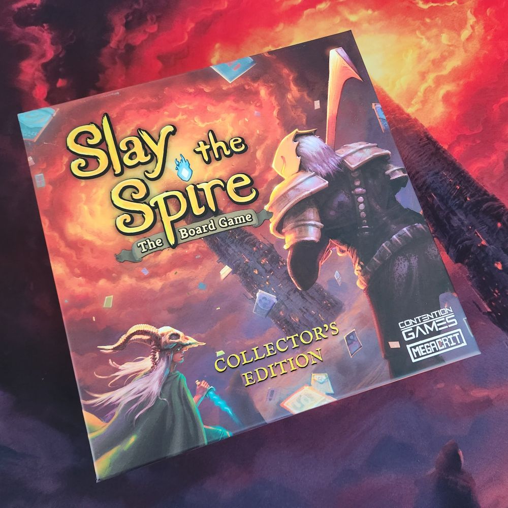 Slay the Spire: The Board Game Collector's Edition.

In the foreground of the cover art, a womam in a green cloak, weilding a dagger of blue energy and wearing a large, horned skull as a helmet accompanies a masked, armored warrior shouldering a heavy, hooked-blade sword toward a towering black spire whose top pierces flame-red stormclouds.