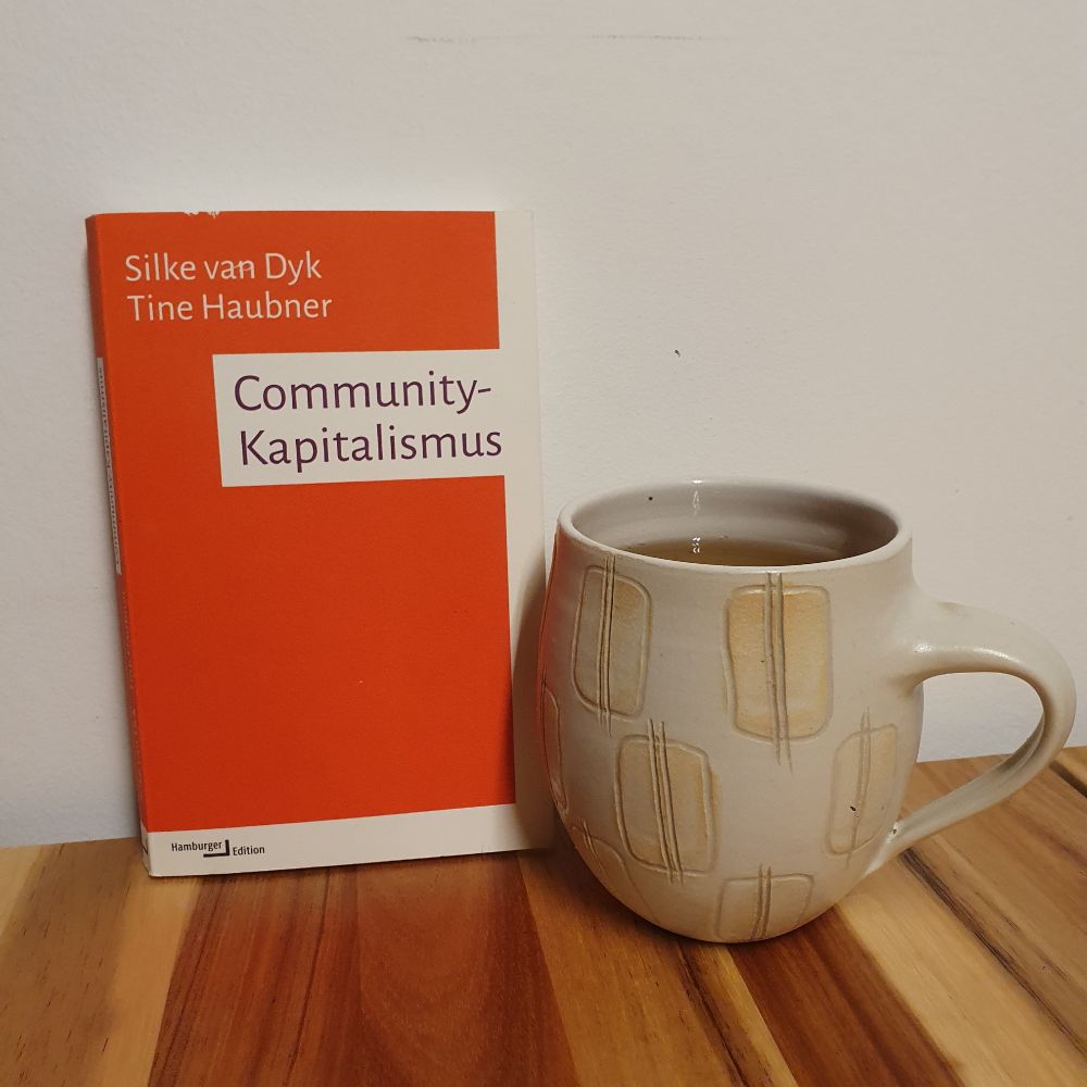 Das Buch "Commyunity-Kaoitalismus" von Silke von Dyk und Tine Haubner neben einer bauchigen getöpferten Tasse.