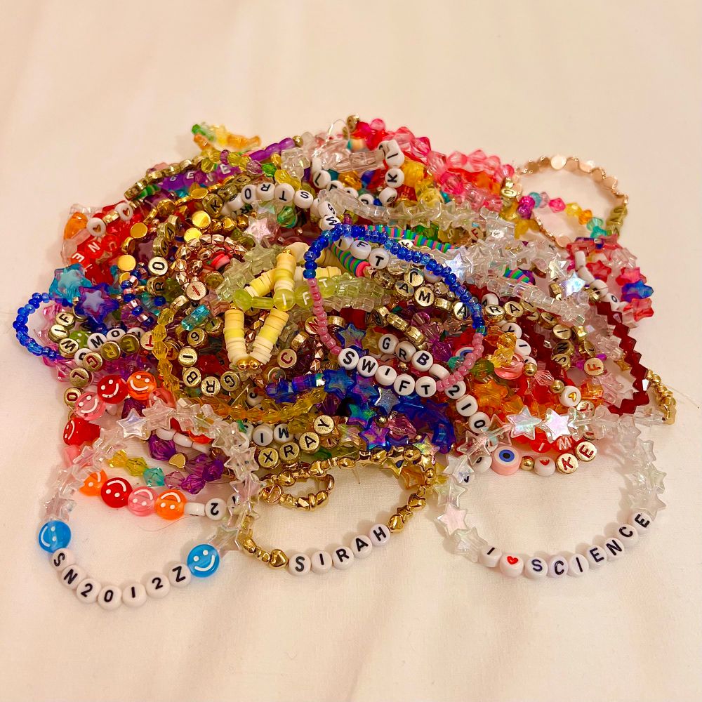 A pile of several colorful friendship bracelets. Three are offset to the front, to show prominence, that say “SN 2012Z,” “SIRAH,” and “I ♥️ Science.”