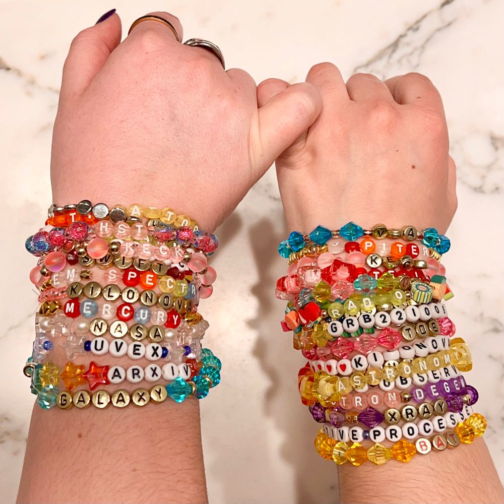 Two hands with several colorful friendship bracelets on the wrists.  The pinkies are linked.