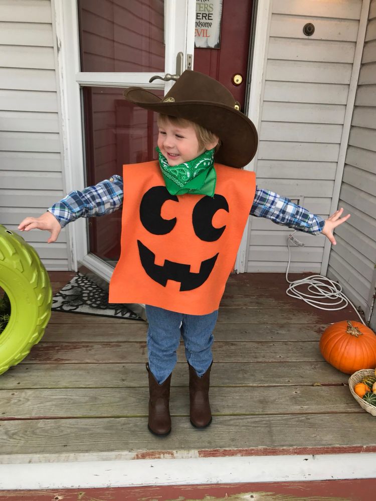 Three year old boy dressed as a cowboy with an orange pumpkin face poncho. 