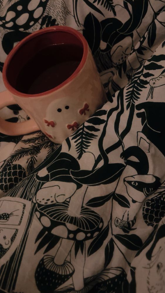 Eine rosafarbene Tasse mit Geist-Print steht auf einer Decke mit Wald Motiv.