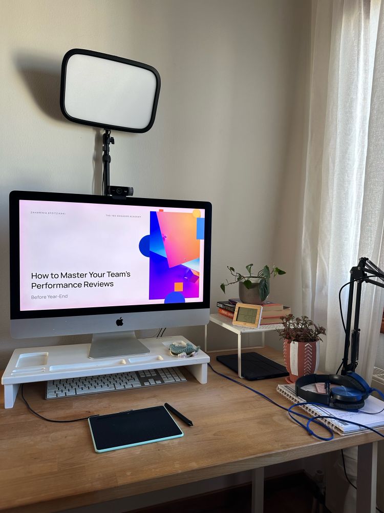 Picture of a desk with an iMac showcasing a performance reviews presentation in full screen. There’s an Envato light above, some plants and various office paraphernalia. 