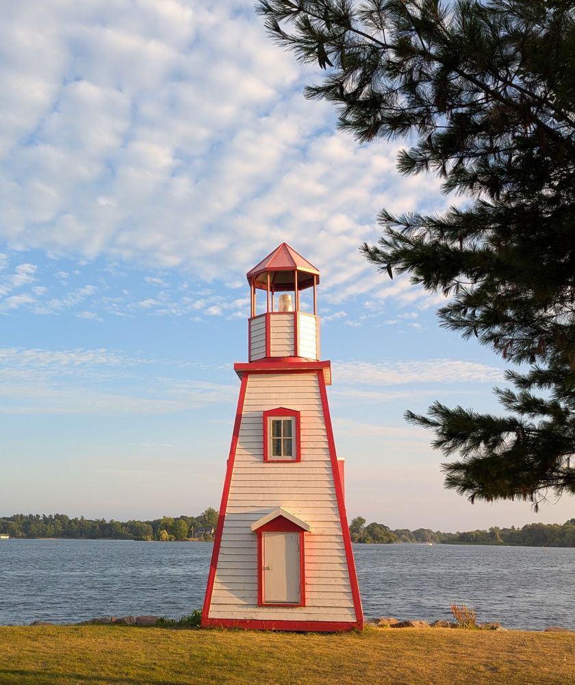 A white lighthouse with red trim on the edge of the St Lawrence River in the town of Gananoque, Ontario 