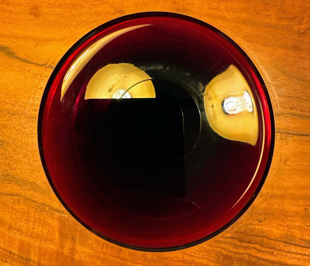 Glass of cheap aussie red wine on a wooden table taken from directly above it. 
It’s such a direct perspective that it just looks like a red-ish circle with bad reflection of ceiling lights in it. 