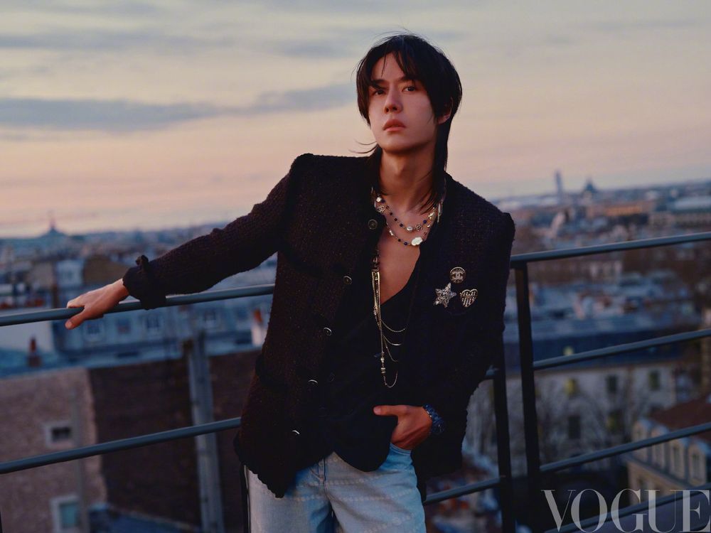 Wang Yibo in Chanel on a Parisian rooftop - holding a bar and leaning forward