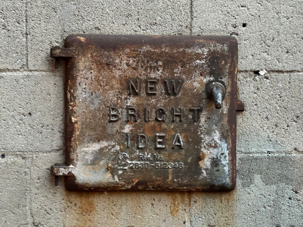 An odd metallic hatchway set into a stone wall. The hatchway is embossed with the words, "New Bright Idea".