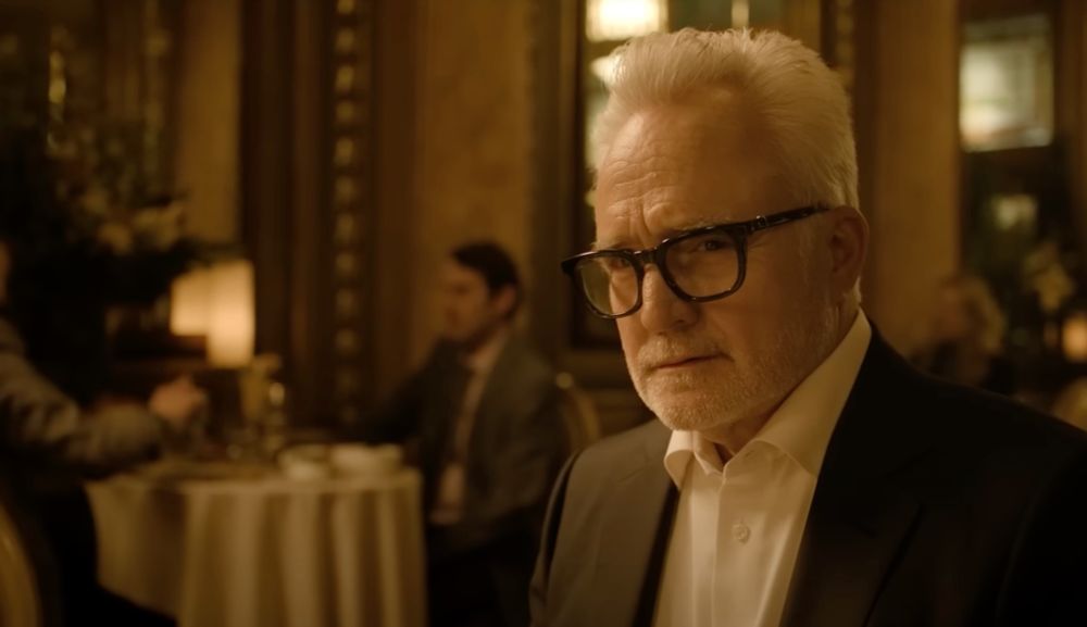 bradley whitford in formal attire, with glasses, in a dimly lit, elegant dining setting