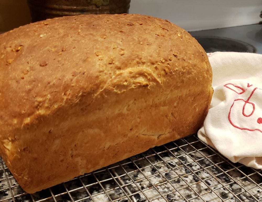 A loaf of bread cools on a rack next to a kitchen towel with an embroidered heart 