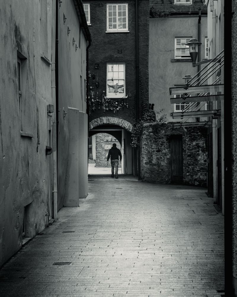 Black and white street photography by Dave Haworth of a man walking down an alleyway in Waterford City Centre, Ireland. 