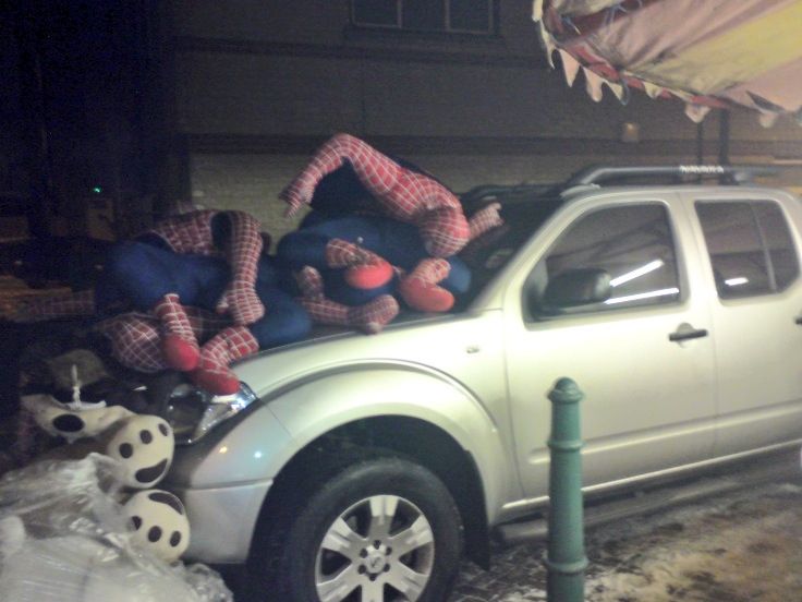 A cluster of spiderman models entangled on a car bonnet in semi-darkness.
