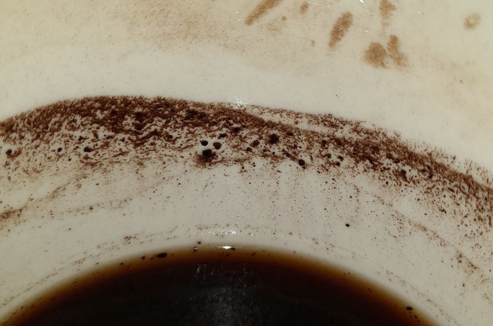 Black coffee grounds making a pattern on inside of mug, looking a bit like canine faces.