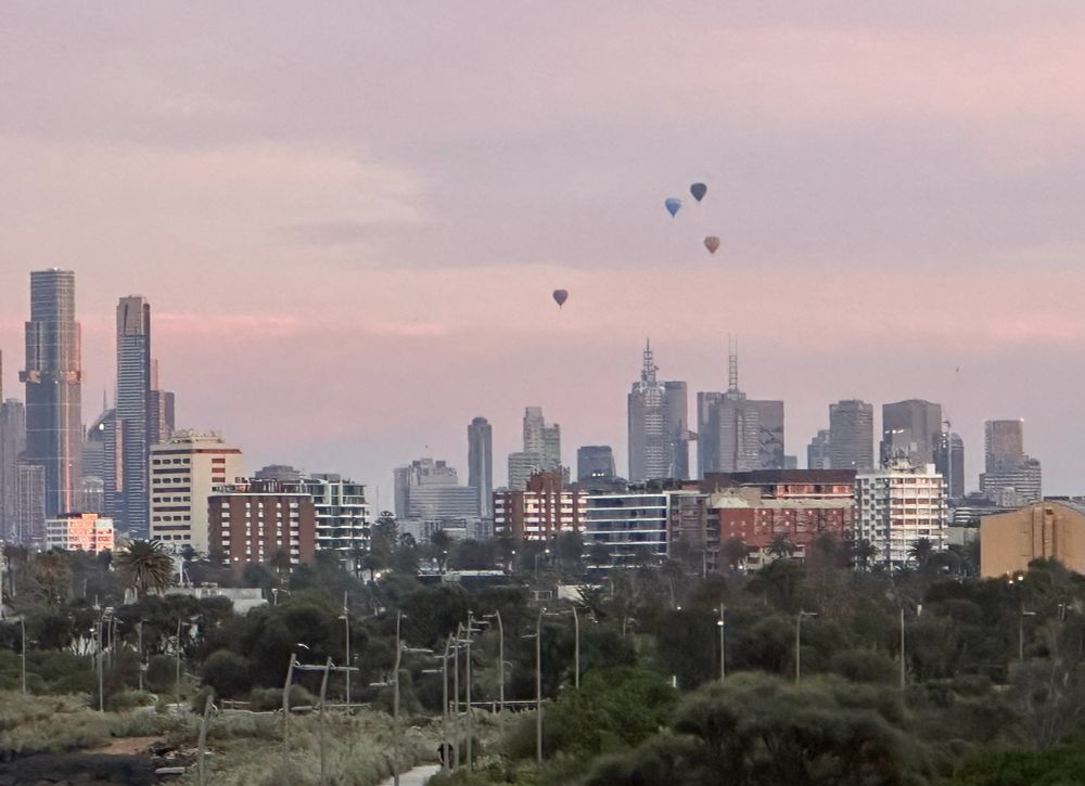 4 hot air balloons flying high behind the city, just on sunrise.