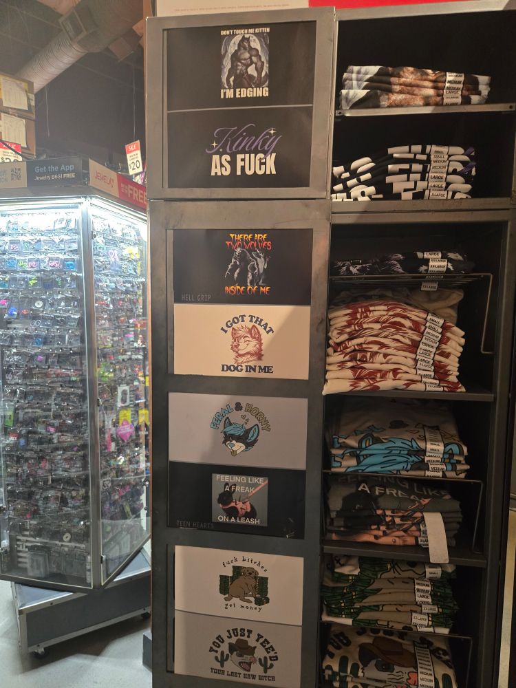 A display of shirts with some obviously furry ones with captions like "I got that dog in me" and "Feral and Horny" with anthro characters on them.