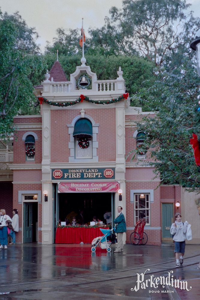 December 1997 photograph of the Fire Station on Main Street, U.S.A. at Disneyland, with Holiday Cookie Decorating available. No historical plaques are present. I happen to be walking away on the right, wearing a Disneyland sweatshirt that would become famous (to me) three months later when I was photographed wearing it as the first dollar customer at Redd Rockett's Pizza Port.