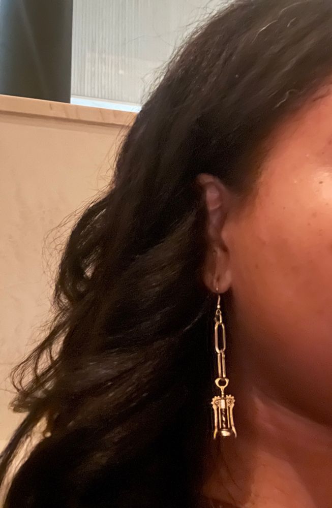 Side of a black woman’s face focused on her earring. The earring is gold with two dangling ovals and a miniature corkscrew that drops just below hew jawline. 