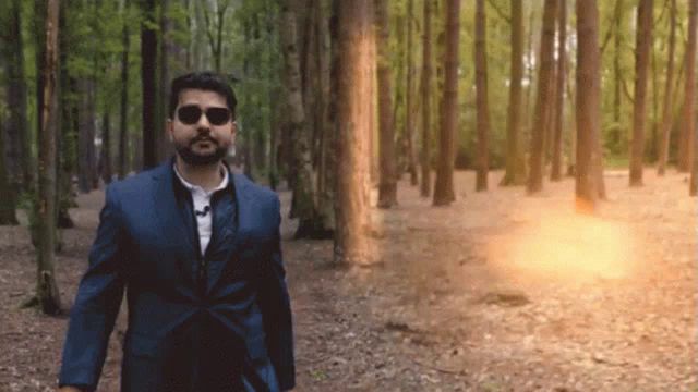 a man in a suit and sunglasses walks through the woods